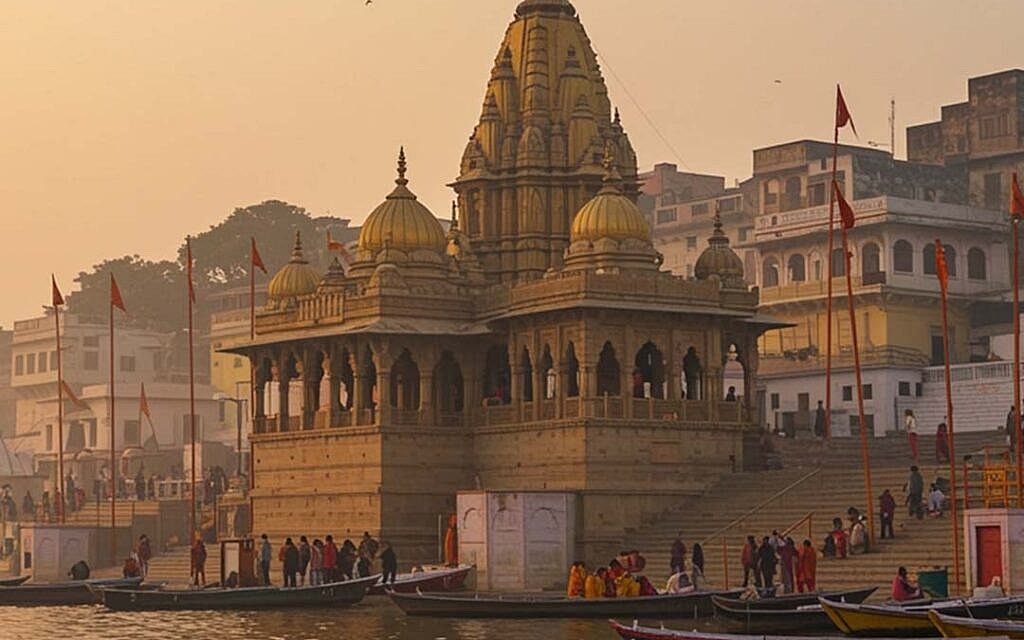 Shri Kashi Vishwanath temple rising above the Varanasi ghats at sunrise, boats moored below